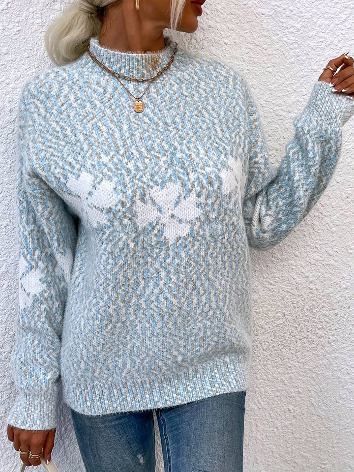 Frau in blau-weißem Strickpullover mit Blumenmuster, Jeans, goldene Halskette.