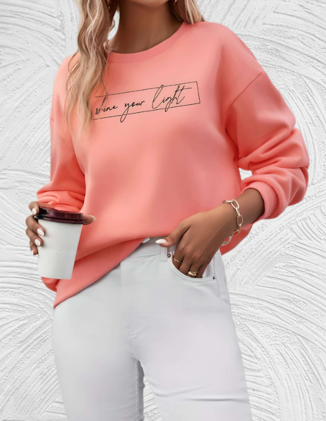 Frau in rosa Pullover mit Schriftzug, hält Kaffeebecher, trägt weiße Hose, modisch, lässig.