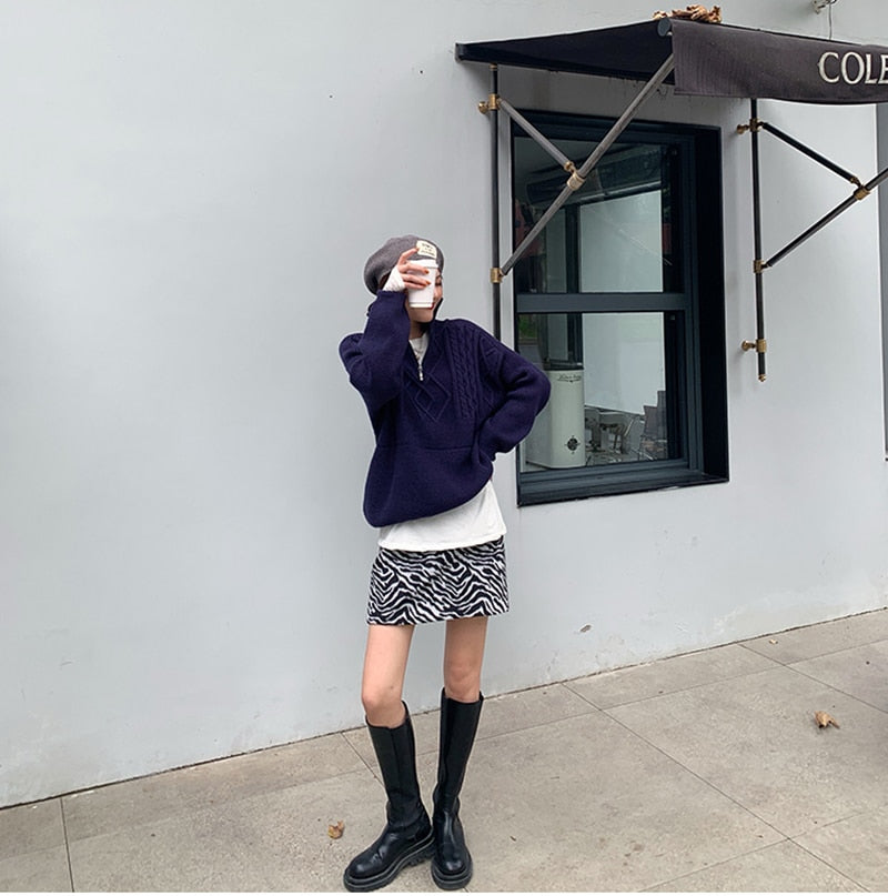 Frau in lila Pullover, Zebra-Minirock, schwarze Stiefel, trinkt Kaffee vor Café.