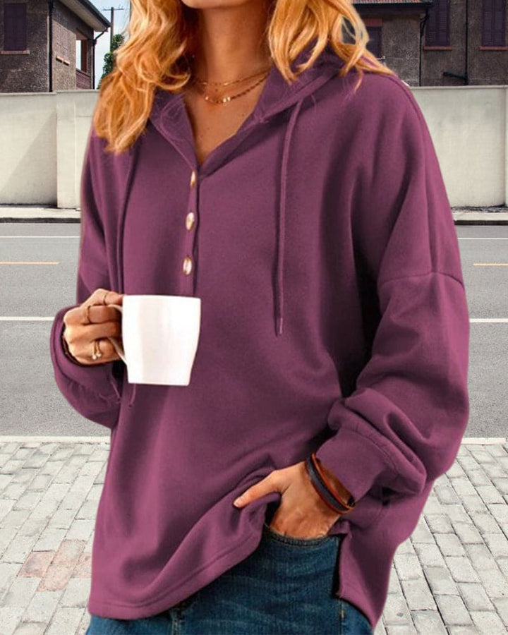 Frau in lila Kapuzenpullover mit Kaffeetasse, lässige Mode, Herbstkleidung, Straße im Hintergrund.