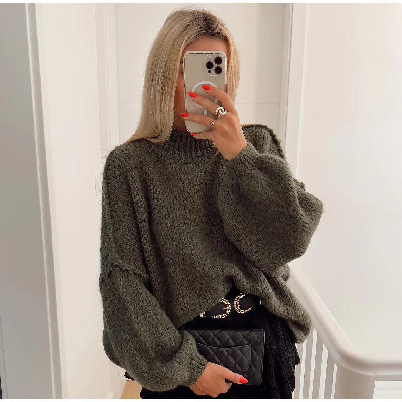 Frau in grünem Strickpullover, hält Smartphone, trägt schwarze Tasche, modisches Outfit.