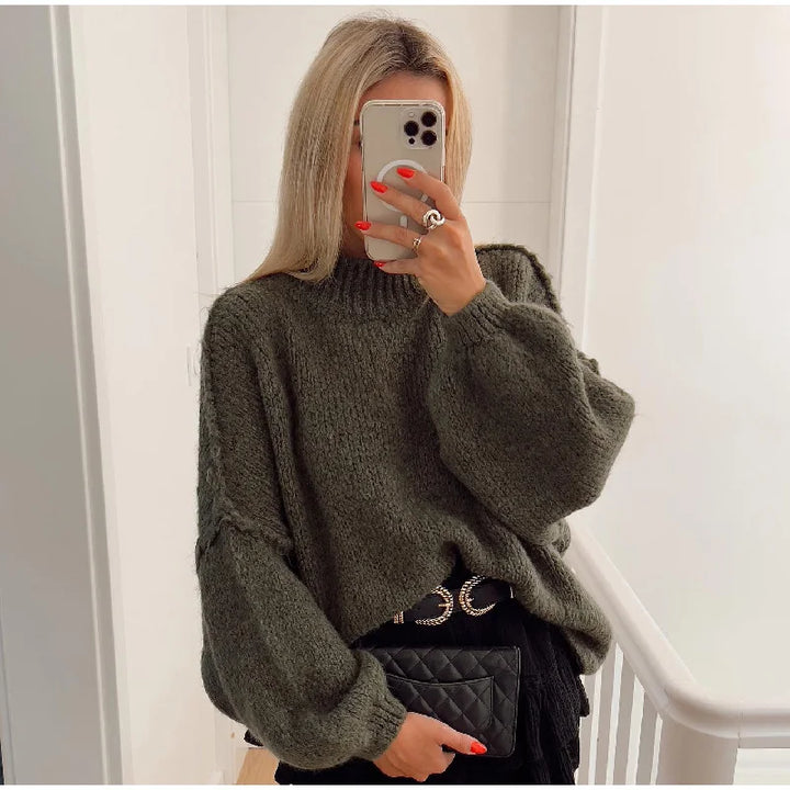 Frau in grünem Strickpullover, hält Smartphone, trägt schwarze Tasche, modisches Outfit.