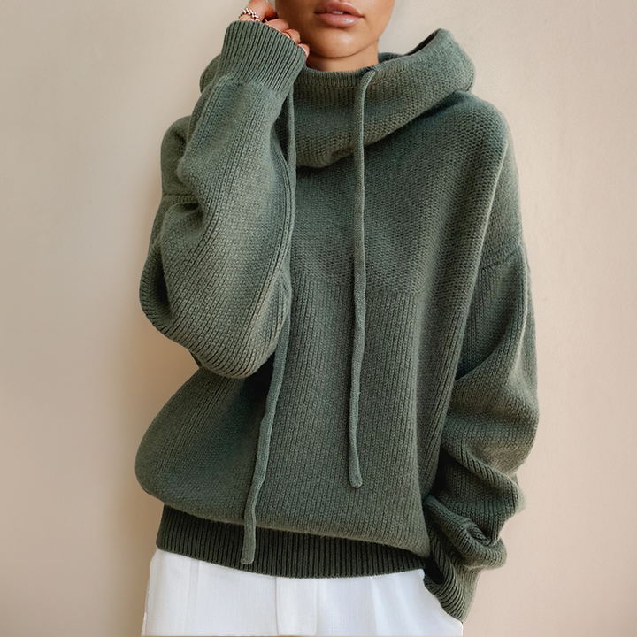 Frau trägt grünen Strickpullover mit Kapuze, Kordeln und weißen Hosen, modisch, gemütlich.