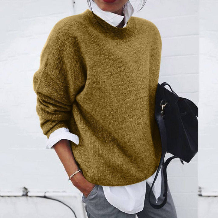 Frau in braunem Strickpullover, weißer Bluse, grauer Hose, schwarze Tasche, lässiger Stil.