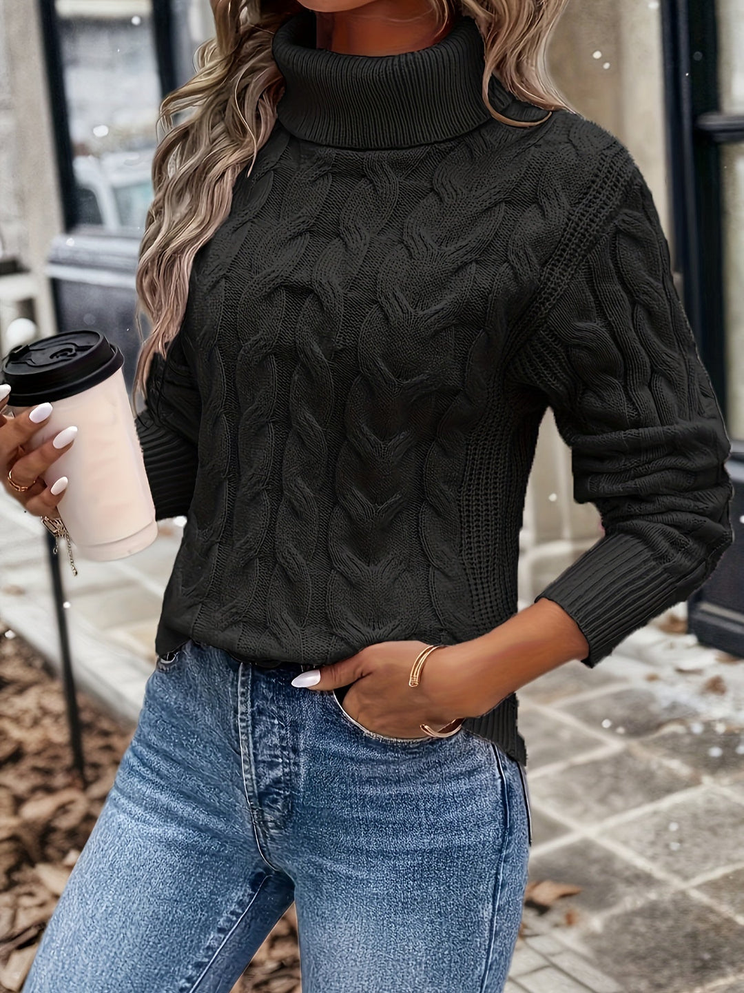 Frau in schwarzem Strickpullover mit Rollkragen, hält Kaffeebecher, trägt blaue Jeans.