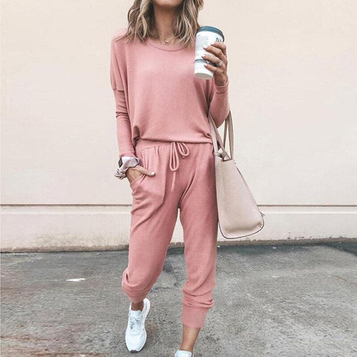 Frau in rosa Freizeitanzug mit Kaffeebecher und beiger Tasche, lässige Mode.