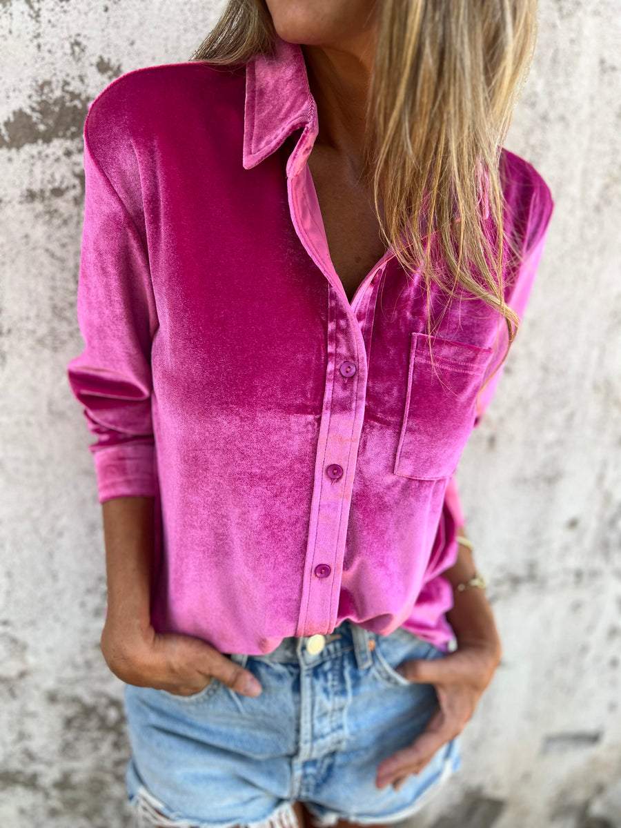 Frau in pinker Samtbluse und Jeansshorts vor Betonwand.