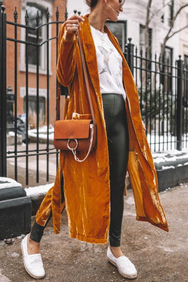 Frau in senfgelbem Samtmantel, Lederleggings, brauner Umhängetasche, weiße Schuhe, Stadtstraße.
