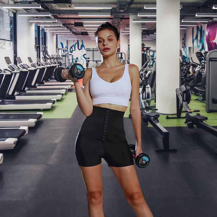 Frau im Fitnessstudio mit schwarzer Sauna-Sweathose und Hanteln, Sportbekleidung, Taille Trainer.