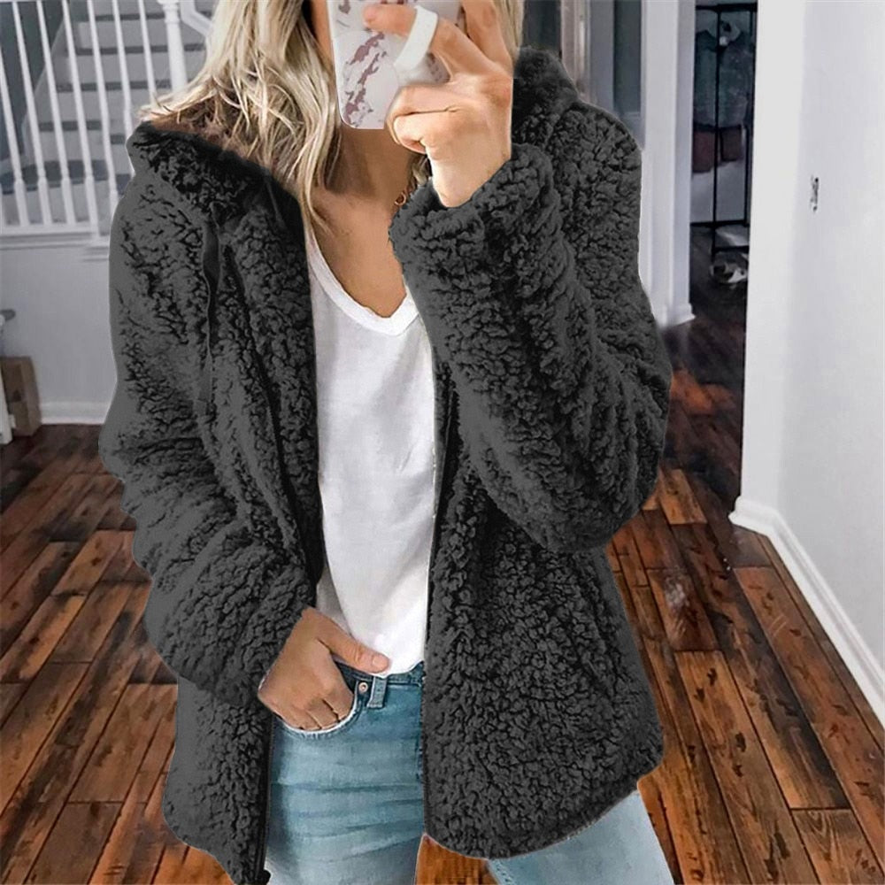 Frau in schwarzer Teddyfelljacke, weißem T-Shirt und Jeans im modernen Innenraum.