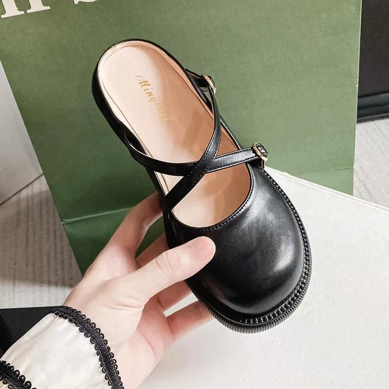Schwarzer Damen-Lederslipper mit Riemen, modisch und bequem, auf grünem Hintergrund.