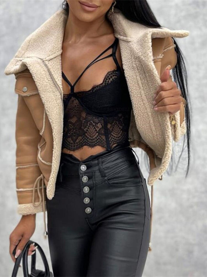 Frau in schwarzem Spitzenoberteil, Lederhose und beiger Jacke mit Schaffellfutter.