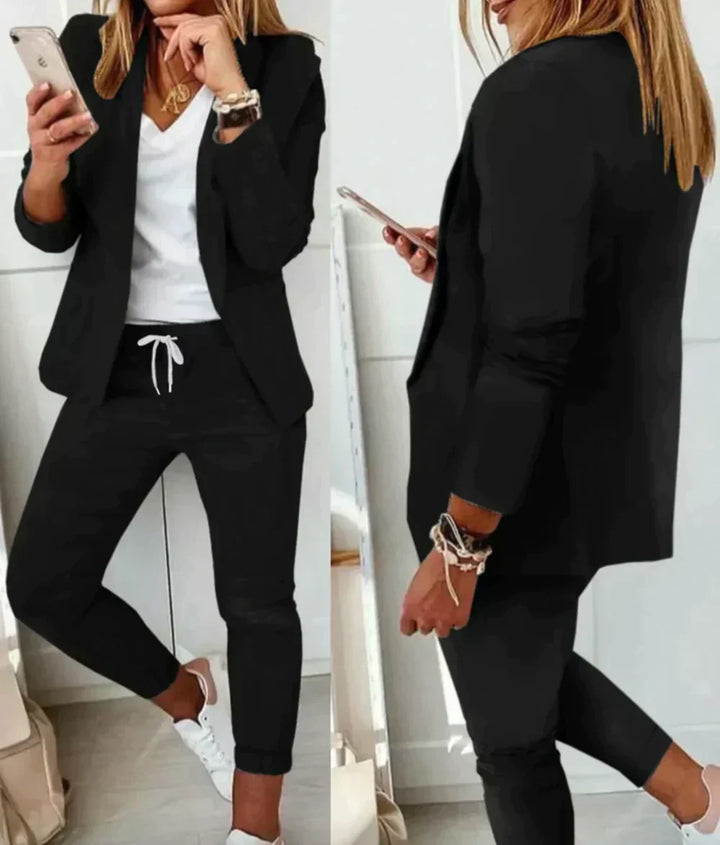 Frau in schwarzem Blazer und Hose, weißes T-Shirt, Smartphone, lässiger Business-Look.