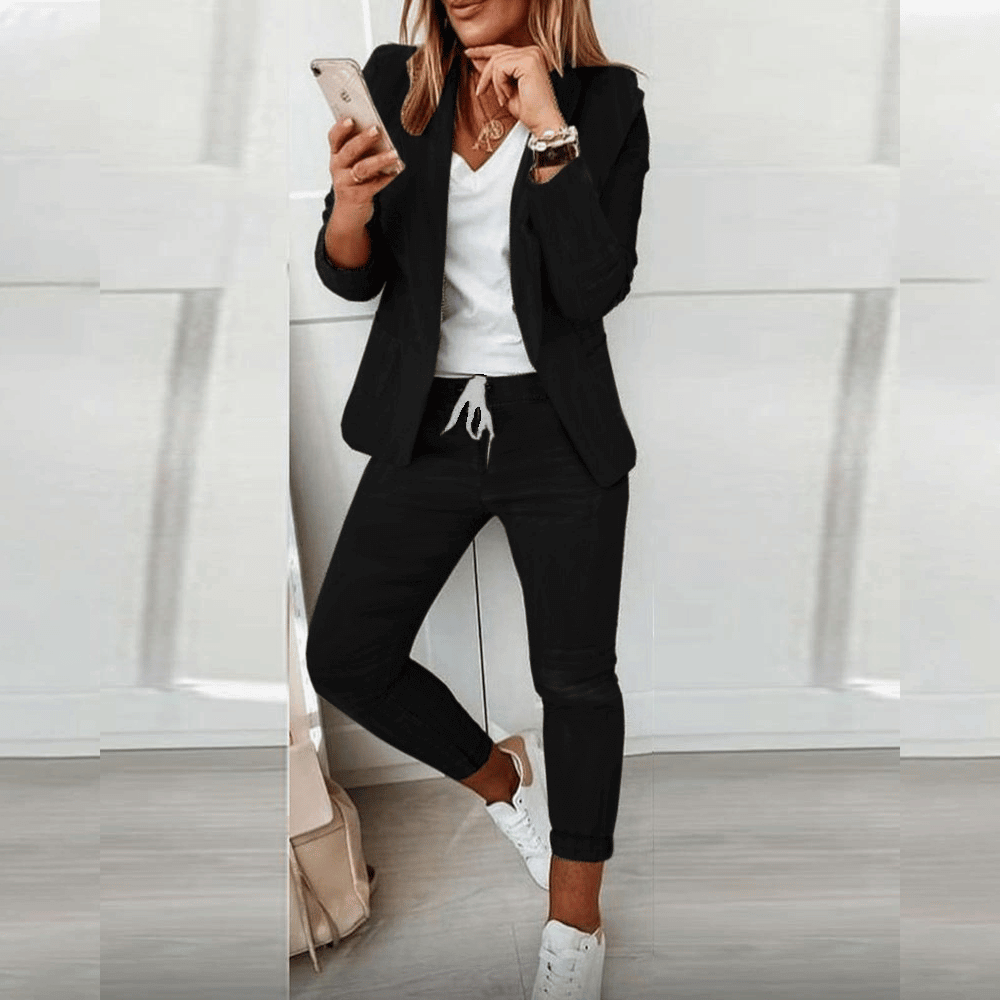 Frau in schwarzem Anzug mit Smartphone, weißem T-Shirt und Sneakers, moderne Businessmode.