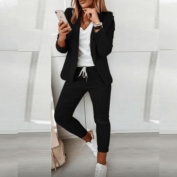 Frau in schwarzem Anzug mit Smartphone, weißem T-Shirt und Sneakers, moderne Businessmode.