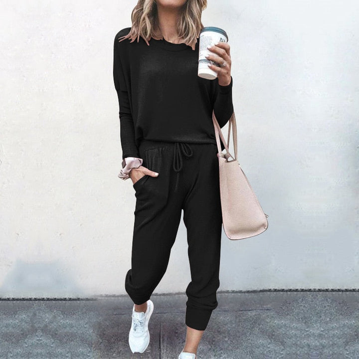 Frau in schwarzem Freizeitanzug mit Kaffeebecher und beiger Tasche, lässige Mode.