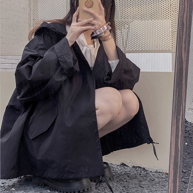 Frau in schwarzem Oversize-Mantel, kniend, mit Smartphone, modisch, urbaner Stil.