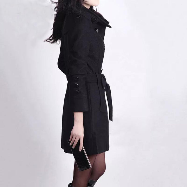 Frau in schwarzem Trenchcoat mit Gürtel, hält Smartphone, modisch, elegant, Herbstbekleidung.