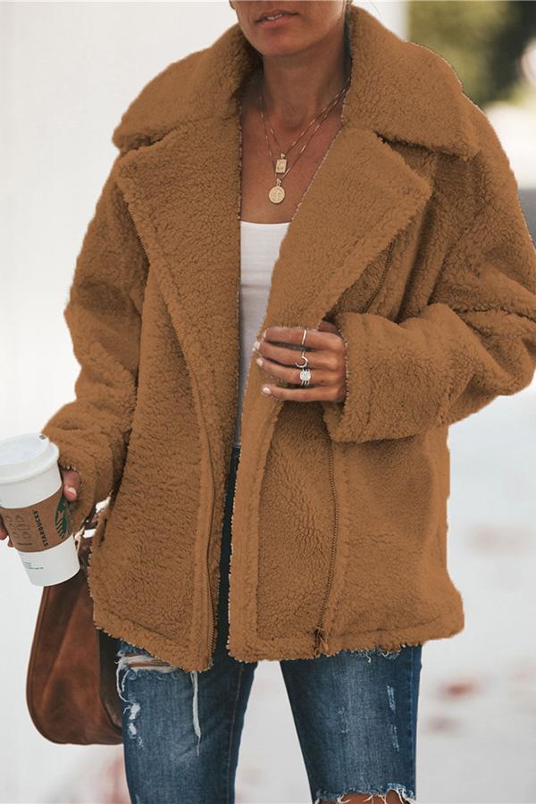 Frau in brauner Teddyjacke, hält Kaffeebecher, trägt Jeans und weiße Bluse.