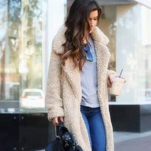 Frau in beigem Teddy-Mantel, grauem Shirt, blauer Jeans, mit Kaffee und schwarzer Tasche.