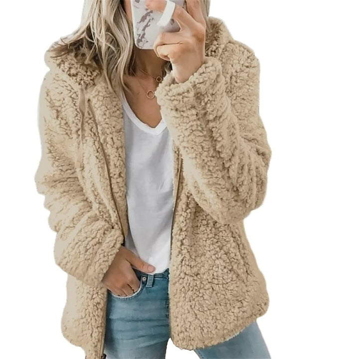 Frau in beigem Teddyfellmantel, weißem T-Shirt, blauer Jeans, Smartphone in der Hand.