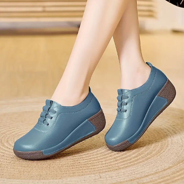 Blaue Damen-Sneaker aus Leder mit Keilabsatz, bequem und modisch, auf Holzboden.