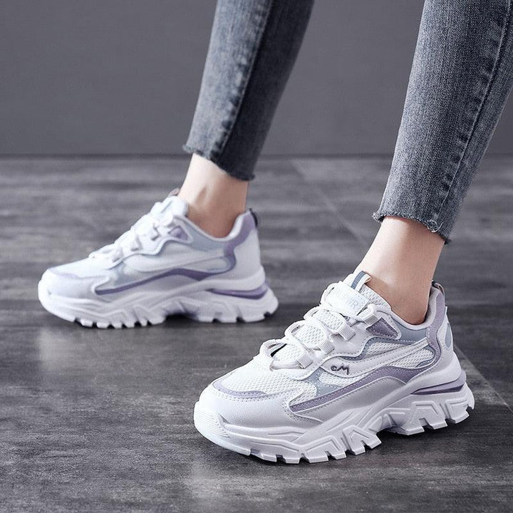 Weiße und lila Damen-Sneaker, klobiges Design, auf grauem Boden.