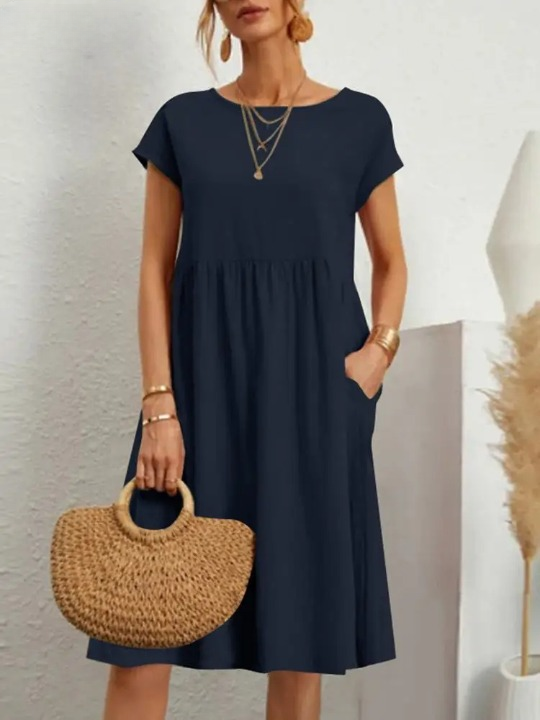 Frau in dunkelblauem Sommerkleid mit Strohtasche, goldenen Accessoires, modisch elegant.