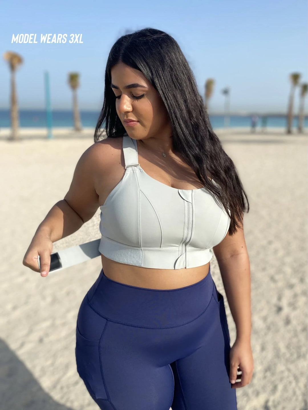 Frau in grauem Sport-BH und blauer Leggings am Strand, Plus-Size-Mode, Fitnessbekleidung.