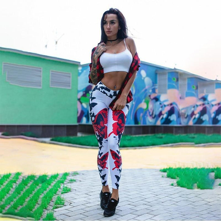 Frau in weißem Sport-BH und gemusterten Leggings vor buntem Gebäude.