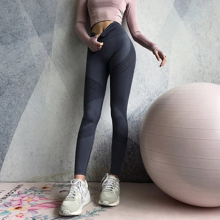 Frau in grauer Sportleggings und rosa Oberteil neben Gymnastikball, Fitnessmode, Indoor-Training.