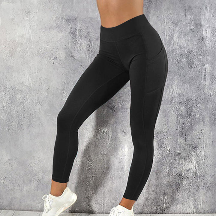 Frau in schwarzer Sportleggings, hohe Taille, vor grauem Hintergrund, Fitnessmode.