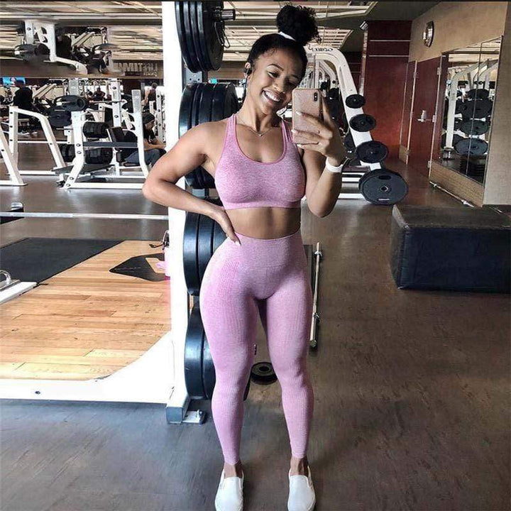 Frau in rosa Sport-Leggings und Top im Fitnessstudio, lächelnd, Selfie machend.