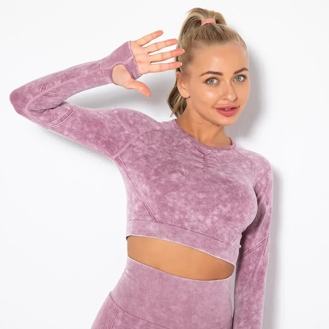 Frau in lila Sport-Set, nahtloses Langarm-Oberteil, Fitnessmode, lächelnd, Hand erhoben.