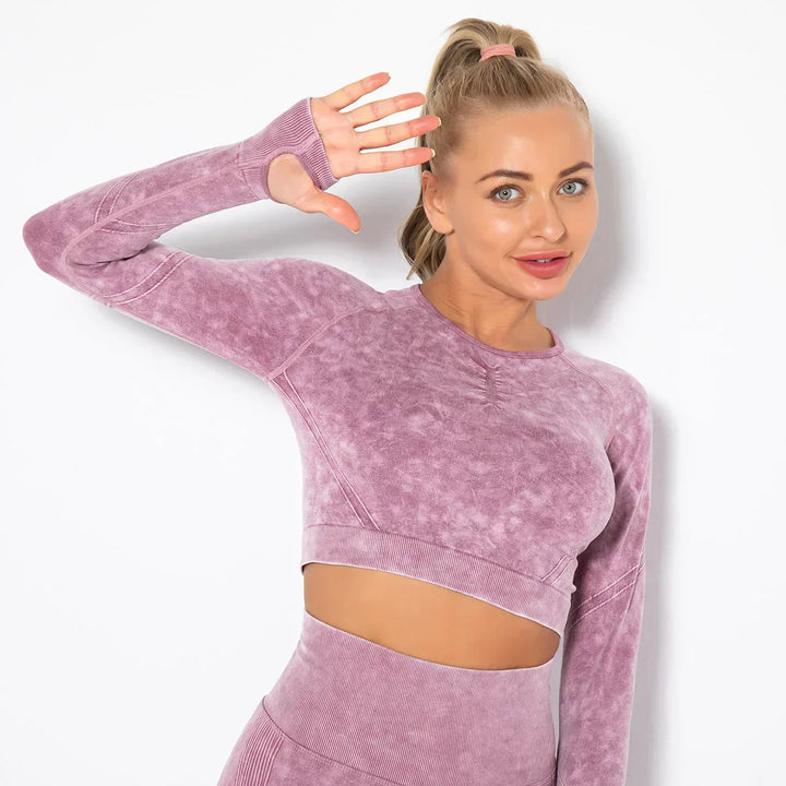 Frau in lila Sport-Set, nahtloses Langarm-Oberteil, Fitnessmode, lächelnd, Hand erhoben.