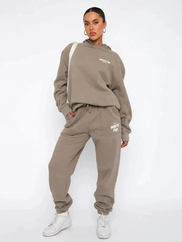 Frau in beigem Hoodie und Jogginghose, sportlich, lässig, Streetwear, weiße Sneaker.