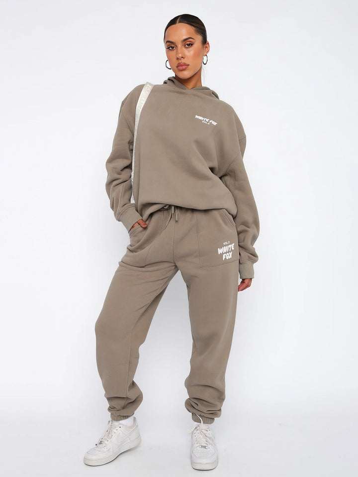 Frau in grauem Hoodie und Jogginghose, sportlich, lässig, Streetwear, weiße Sneaker.