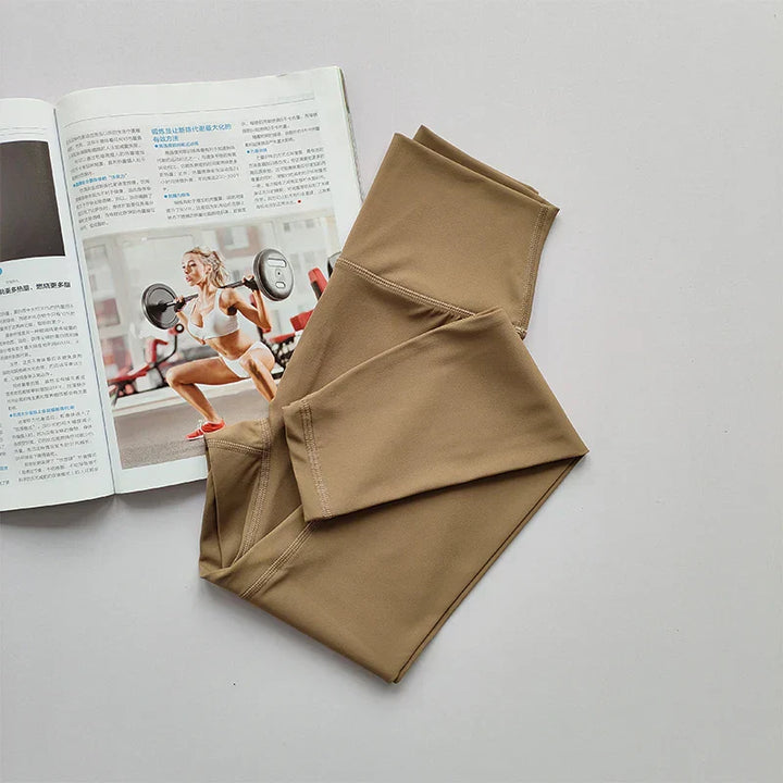 Beige Sportleggings auf weißem Hintergrund neben Fitnessmagazin mit Frau beim Gewichtheben.
