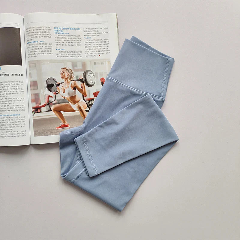 Hellblaue Sportleggings aus Stretchmaterial neben Fitnessmagazin auf weißem Hintergrund.