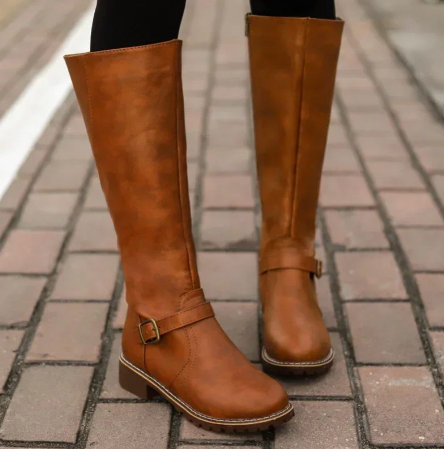 Braune Damenstiefel aus Leder mit Schnalle, kniehoch, auf gepflastertem Gehweg.