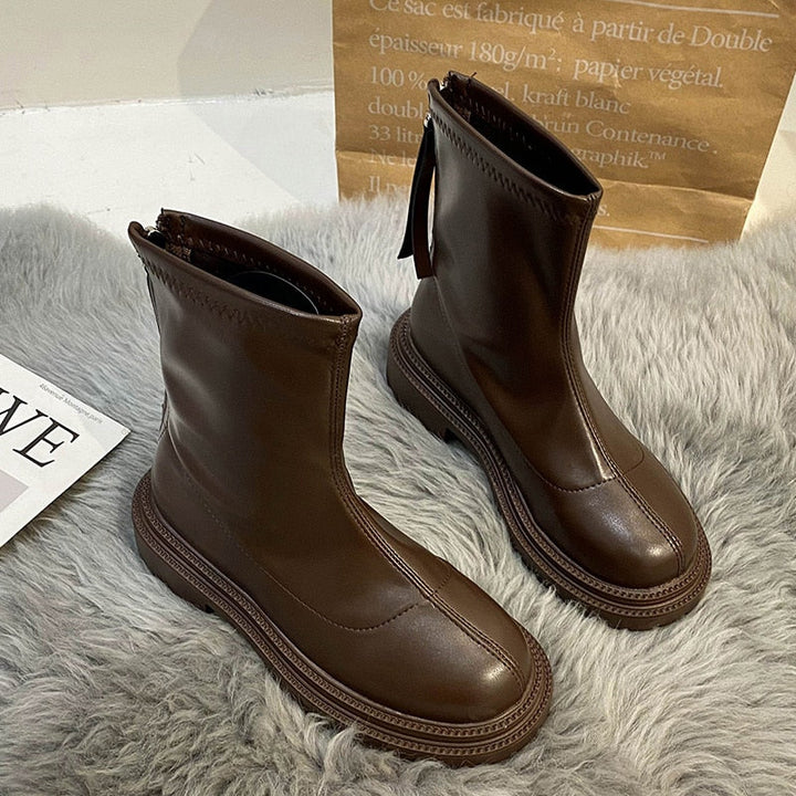 Braune Lederstiefel mit Reißverschluss auf grauem Teppich, modisch und robust.