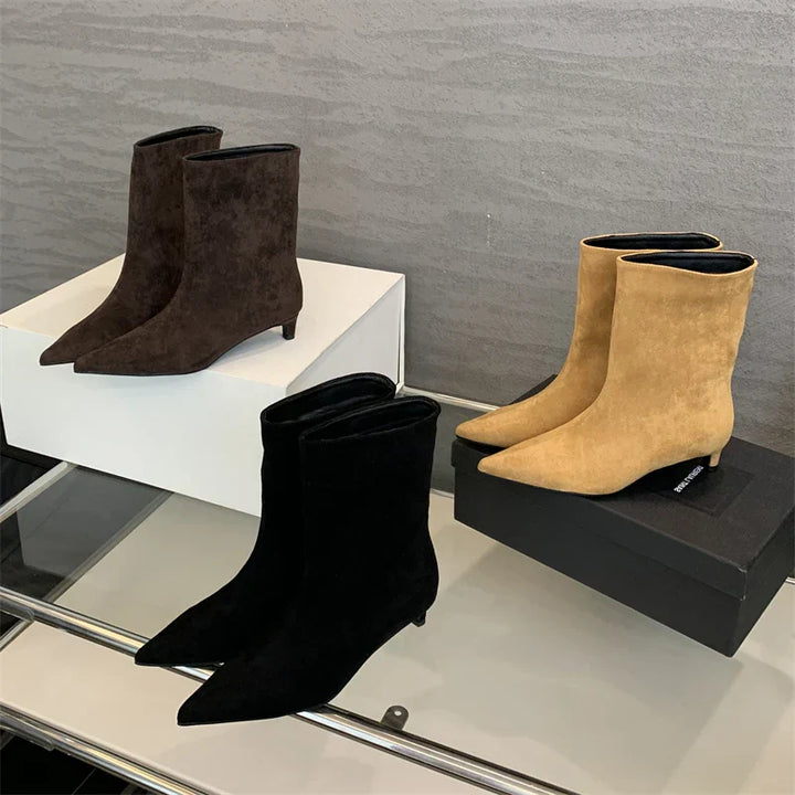 Drei Paar Stiefeletten aus Wildleder in Schwarz, Braun und Beige auf Glasregal.