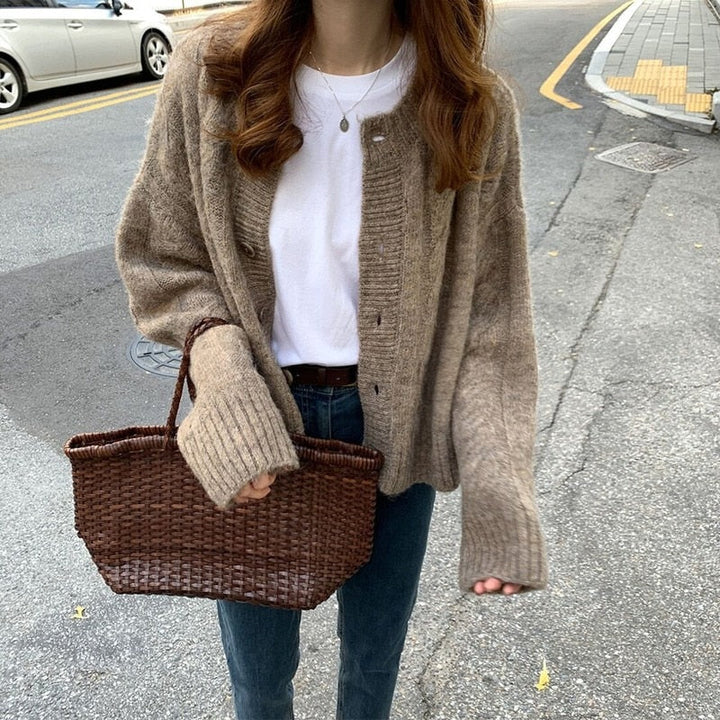 Frau mit braunem Strickcardigan und geflochtener Tasche auf Straße, lässiger Herbstlook.