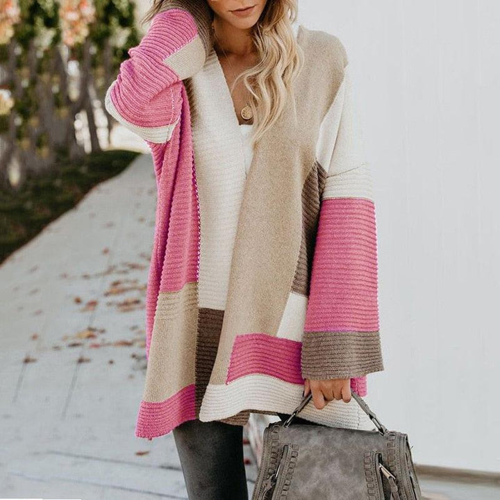 Frau in rosa-beige-weißem Strickponcho, hält graue Handtasche, Herbstmode.