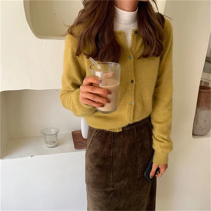 Frau in gelbem Strick-Cardigan mit Knöpfen, hält ein Glas Kaffee, lässiger Herbst-Look.