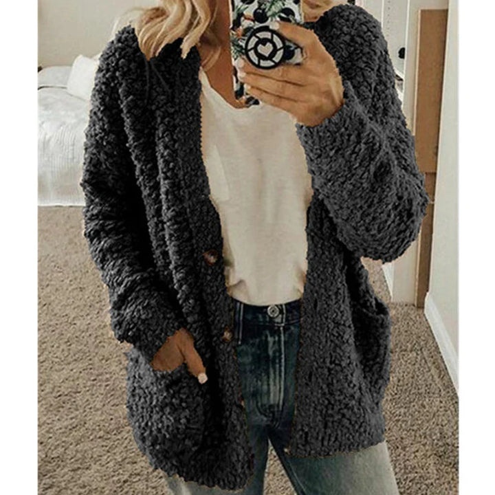 Frau in grauem Strick-Cardigan, weißem T-Shirt und Jeans, hält Smartphone, gemütlicher Look.