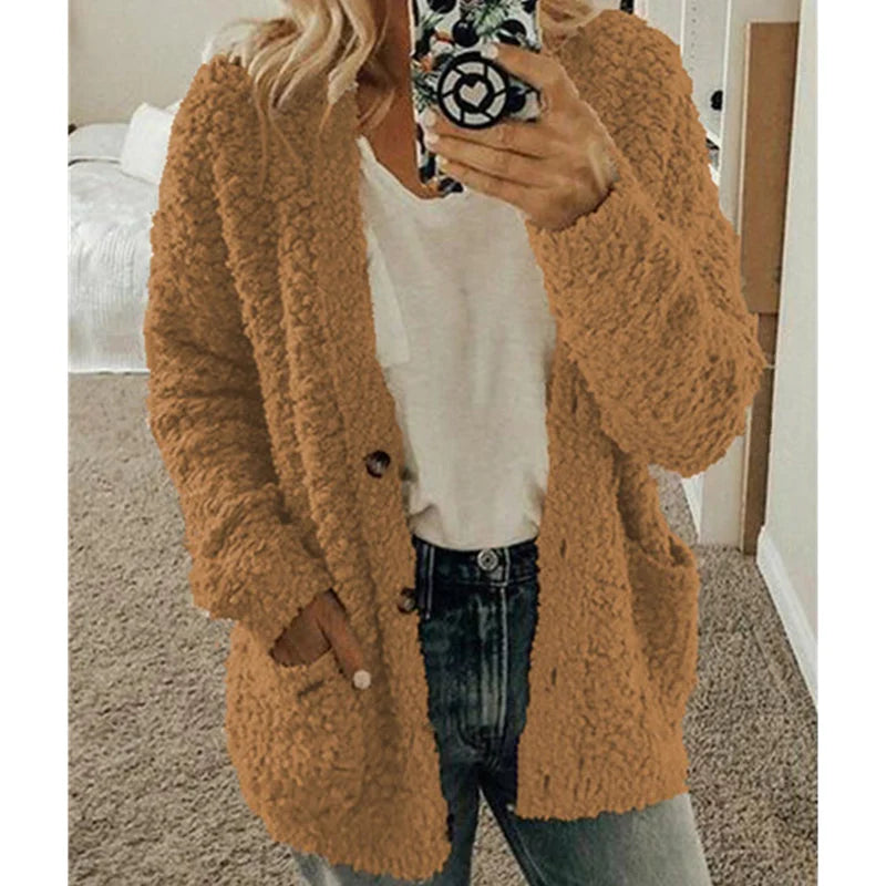 Frau in beigem Strickcardigan, weißem T-Shirt und Jeans, Selfie im Schlafzimmer.