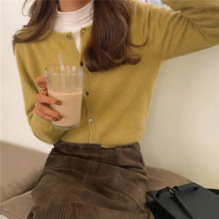 Frau in gelbem Strick-Cardigan mit Getränk, brauner Rock, lässiger Herbstlook.
