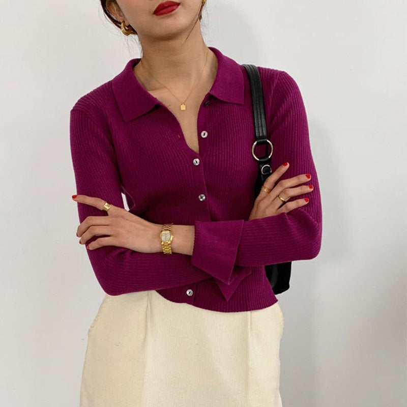 Frau in lila Strickjacke mit Knöpfen, weißem Rock, schwarzer Tasche, modisch, elegant.