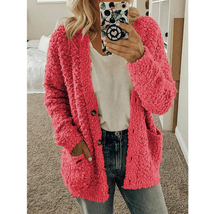Frau in rosa Strickjacke, Handyhülle mit Muster, lässiger Look, gemütliches Wohnzimmer.